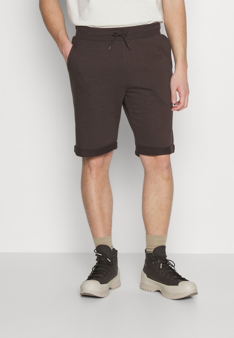 Brown cotton shorts with a drawstring waist, rolled cuffs, and side pockets, paired with grey high-top shoes and tan socks.