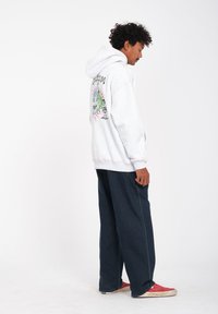 Gray hoodie with a graphic on the back featuring a colorful design. Paired with dark loose-fitting jeans and red sneakers.