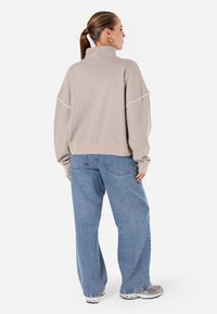 Beige, teksturert genser med høy krage og hvite sømmer, sammen med lyseblå baggy-jeans. Fottøyet inkluderer grå joggesko.