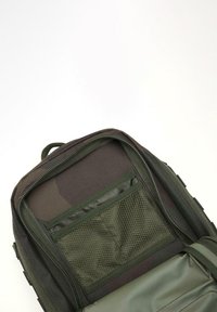 Zöld vászon hátizsák belső része cipzárral, hálós zsebbel és oldalzsebbel, texturált anyaggal és megerősített varratokkal.