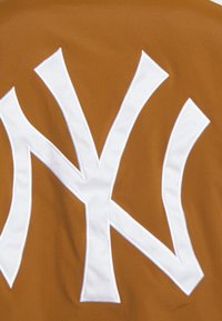 Brun tyg med en stor vit broderad "NY"-logotyp med förlängda, vinklade former; slät textur med en enfärgad bakgrund.