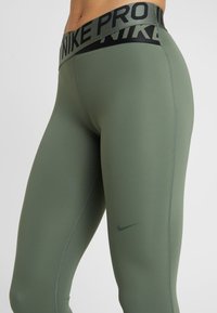 Nike Pro legging in olijfgroen, met een hoge tailleband met zwarte "NIKE PRO" tekst, gladde stof, aangesloten ontwerp en subtiele logodetail.