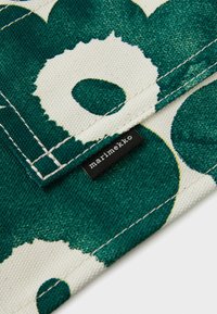 Zöld és fehér virágmintás pamut anyag; látható varrással és fekete "marimekko" címkével rendelkezik.