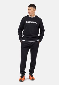 Felpa navale con testo bianco "ROSSIGNOL", abbinata a pantaloni coordinati e scarpe da ginnastica arancioni. Design casual; materiale in cotone, polsini a costine.