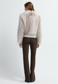 Chaqueta recortada de felpa en suave rosa con un acabado texturizado, cuello alto y dobladillo acanalado, combinada con pantalones marrones ajustados.