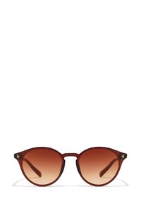 Pyöreät aurinkolasit, joissa on laikullinen ruskea kehys, liukuvärjätyt ruskeat linssit ja mustat yksityiskohdat temppeleissä. Ominaisuutena tyylikäs, minimalistinen muotoilu.