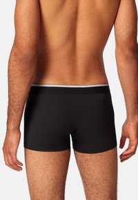 Boxer-briefs noirs avec un design ajusté, en tissu doux, et une ceinture grise contrastante, mettant en avant une texture lisse et des lignes épurées.