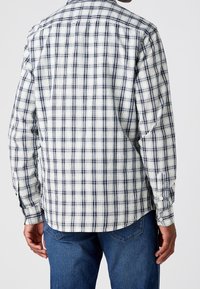 Lange mouwen shirt met een wit- en marineblauw ruitpatroon, gemaakt van geweven stof met manchetten met knopen en een afgeronde zoom. Achteraanzicht getoond.