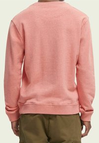 Rosa sweatshirt med rund hals, ribbade ärmslut och nederkant, mjuk textur och minimala sömnadsdetaljer, bärs över gröna shorts.