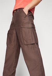 Pantalones cargo marrones hechos de una tela duradera, con dos grandes bolsillos laterales, detalles de costura y un ajuste relajado.
