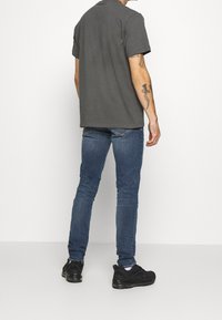 Grå bomullströja med korta ärmar, tillsammans med blå denimjeans och svarta sneakers, som visar en avslappnad passform och diskreta sömdetaljer.