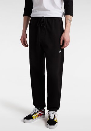 Pantaloni della tuta neri con vita elastica e polsini; presenta un piccolo logo bianco sulla coscia sinistra. Abbinati a sneakers Vans multicolori.