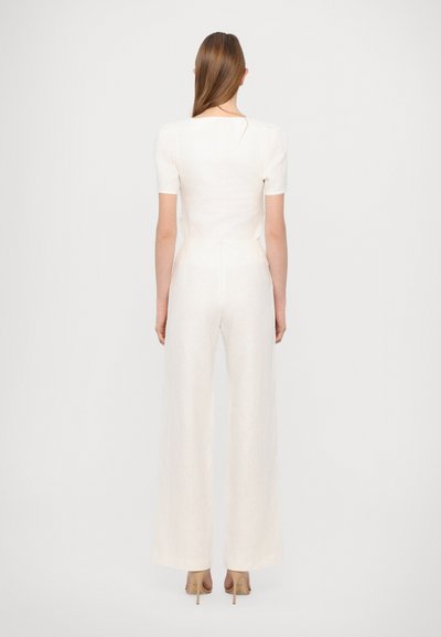 Kermanvärinen pellavajumpsuit, jossa on lyhyet hihat, neliömäinen takaosa ja leveät lahkeet. Sileä pinta, jossa on piilotettu vetoketju.
