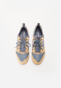 Niebieskie i beżowe buty sportowe z siateczkową cholewką, zamszowymi akcentami, okrągłymi sznurówkami oraz pętlą na pięcie ułatwiającą zakładanie.