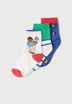 Three colorful children's socks: white with bear skier and red toe, white/blue stripes with green cuff, and blue with red cuff and flags.