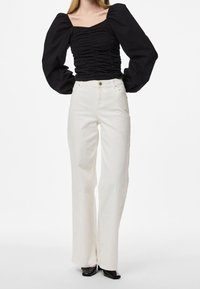 Haut noir froncé avec encolure carrée et manches volumineuses, associé à un pantalon blanc à jambes larges avec fermeture à boutons et fermeture éclair à l'avant.