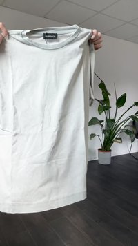 Svetlo siva kratka majica s kratkimi rokavi, ki je prikazana, ima okroglo ovratnico, mehak bombažni material in ravni rob. Oznaka je vidna na ovratniku.