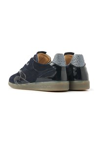 Ein Paar marineblaue Wildledersneaker mit glänzenden schwarzen Akzenten, strukturierten Fersenlaschen, beige Innenauskleidung und Gummisohlen, die mit "VIA VAI" geprägt sind.