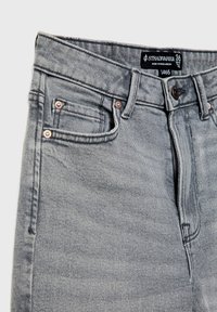 Vaqueros de mezclilla gris con una cintura alta, cinco bolsillos y remaches de cobre; incluye una etiqueta negra con información de la marca y tamaño.