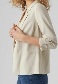 Lichtbeige blazer met een reverskraag, enkele knoop aan de manchetten en zijzak. Soepele textuur en een ontspannen pasvorm.