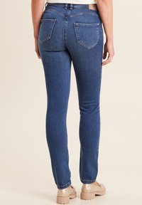 Schmale Blue Jeans aus Denim mit normaler Taille, zwei Gesäßtaschen und Auswaschungen entlang der Beine. Kombiniert mit hellbraunen Schuhen.