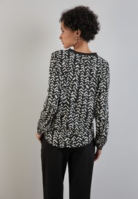 Blusa a righe bianco e nero con forme di frecce astratte, maniche lunghe con polsini elasticizzati e orlo arrotondato.
