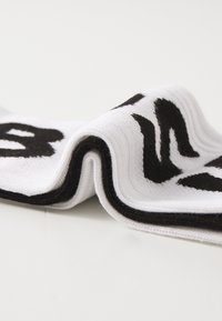 Chaussette en coton blanc avec une surface texturée, arborant des lettres noires en gras et une bande noire contrastante en haut.