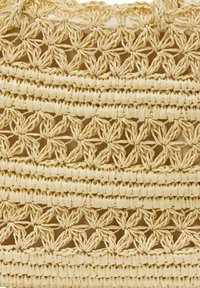 Bolso de paja tejido con intrincados patrones en forma de estrella, alternando secciones sólidas y abiertas. Color beige claro con una superficie texturada.