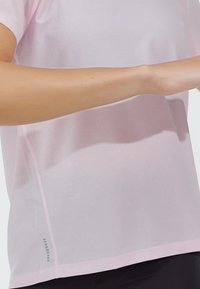 Camiseta atlética de malla rosa claro con mangas cortas, que presenta un diseño texturizado y una etiqueta "AEROREADY" en la costura lateral inferior.