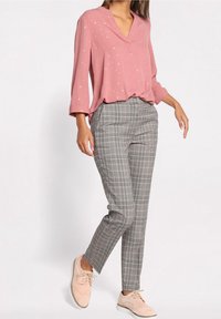 Blouse rose avec un col en V et de petits motifs floraux, associée à un pantalon gris à carreaux fuselé et des chaussures oxfords rose clair.