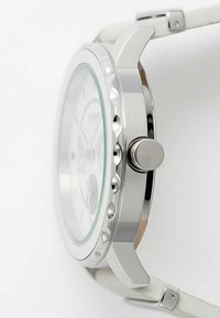 Silberfarbene Uhr mit einem runden Gehäuse, einem strukturierten Rahmen, einem weißen Lederarmband und einem klaren Glaszifferblatt, das silberne Zeiger und Markierungen zeigt.