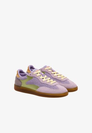 Paire de baskets lavande et vertes avec des lacets beige et des semelles en caoutchouc marron sur fond blanc.