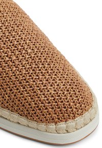 Espadryle z plecionym słomkowym wykończeniem w odcieniu brązowym, z białą gumową podeszwą i obszytym beżowym wykończeniem wokół palców.