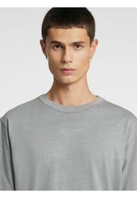 Grå oversized t-skjorte laget av mykt stoff. Har rund hals og subtilt trykt tekst på øvre front. Sømløse korte ermer.