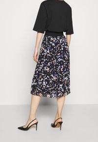 Černé tričko spojené s plisovanou midi sukní s vícebarevným květinovým vzorem v modré, bílé a růžové, doplněné černými vysokými podpatky.