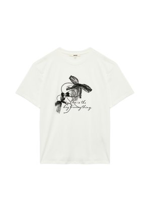 Camiseta blanca de algodón que presenta lazos de encaje negro y un texto decorativo que dice: "El amor es la clave de todo" en una fuente cursiva.