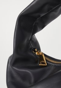 Musta nahkainen käsilaukku, jossa on teksturoitu, pehmeä pinta. Laukussa on kultaiset vetoketju ja metalliosat, ja sen muoto on löysä ja kaareva.