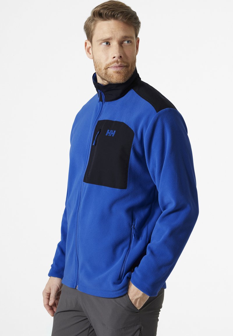 Blaues Fleece-Jacke mit schwarzen Schulterakzenten, hochgeschlossenem Kragen und Reißverschluss-Brusttasche. Verfügt über eine glatte Textur und ein schlichtes Design.