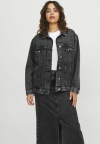 Zwarte denimjas met een knoopsluiting aan de voorkant, zijzakken en een relaxte pasvorm, gecombineerd met een zwarte denimrok met een split aan de voorkant.