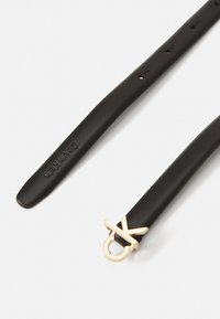 Bracelet en cuir noir avec un accent en métal doré et un détail de boucle distinctif, ainsi que plusieurs trous de réglage pour personnaliser la taille.