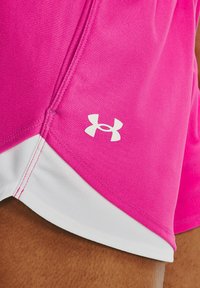 Primer plano de pantalones cortos deportivos rosas y blancos con el logo de Under Armour, usados en piel morena.