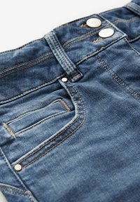 Tummansiniset farkut, joissa on sileä pinta, hopeiset metallinapit, erottuva ommel ja takatasku.