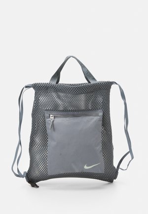 Szary pleciony plecak na sznurki z przednią kieszenią na zamek i małym logo Nike na kieszeni, na jednolitym białym tle.