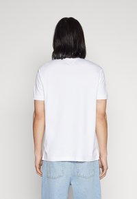 Maglietta di cotone bianca con maniche corte, collo a giro e un leggero dettaglio a forma di V sul retro. Indossata con jeans azzurri chiari.