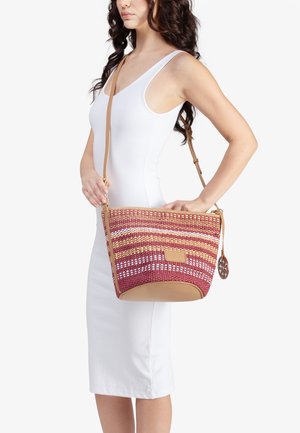 Donna con vestito bianco senza maniche che porta una borsa a tracolla intrecciata rosa e beige con motivo a righe e dettagli in pelle.