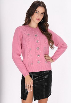 Pulover tricotat roz cu guler rotund, având modele cu cabluri și strasuri decorative. Poartă-l cu o fustă mini din piele neagră.