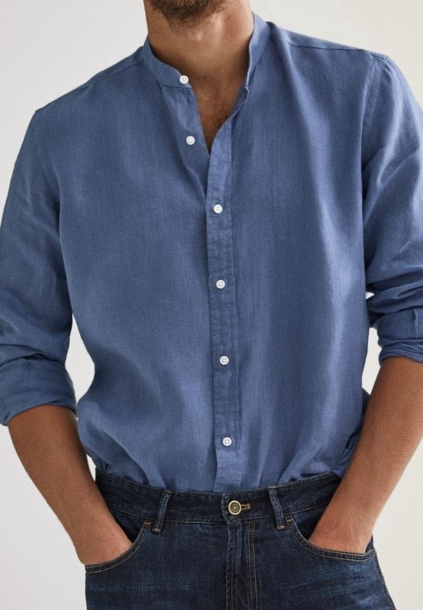 Lichtblauwe, langromp shirt met een opstaande kraag, knoopsluiting aan de voorkant en een zachte textuur. Gecombineerd met donkere spijkerbroek.