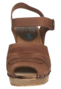 Sandale à talon compensé en cuir brun avec un bout ouvert, sangle de cheville réglable, design de sangle décorative et rivets métalliques sur la semelle.