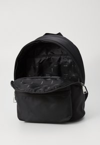Black backpack made of smooth nylon with a zippered closure, featuring an interior compartment lined with a subtle logo pattern.