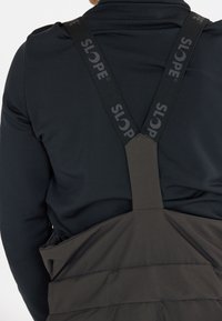 Svart långärmad skjorta med justerbara svarta remmar märkta "SLOPE" och ett mörkgrått överlager med en texturerad yta, med en lös passform.